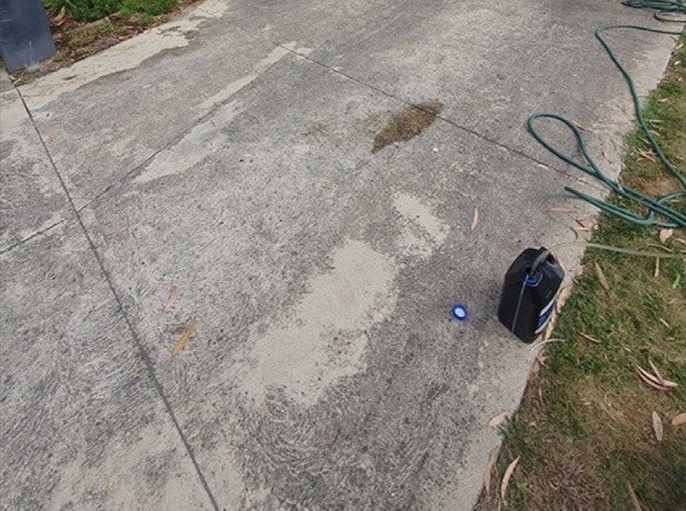 A concrete driveway mottled grey with dirt and staining, with a hose run out across it