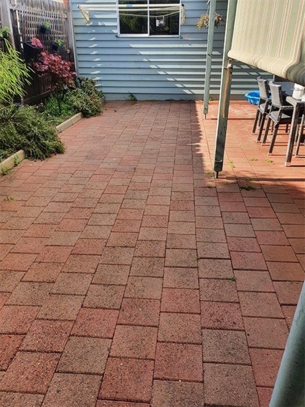 The same pavers washed back to clean red brick, under the awning beside the blue weatherboard wall