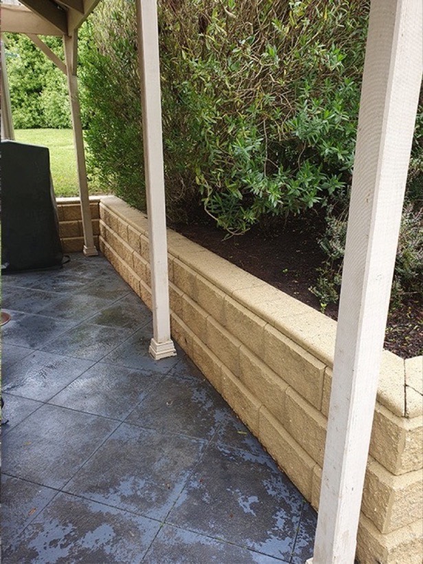 The same patio and retaining wall after washing, with the moss off the blocks and the tile colour back