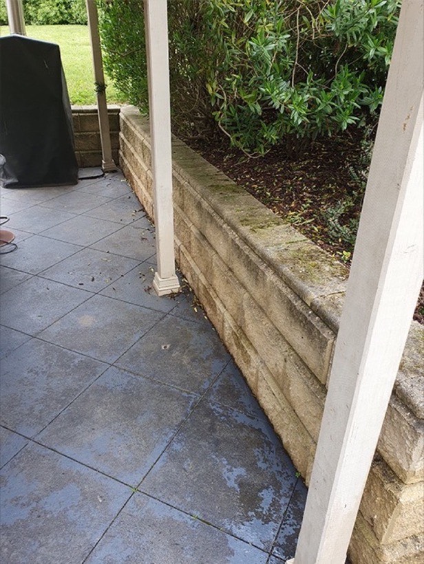 A tiled patio and retaining wall under a verandah, dulled and darkened with dirt before cleaning