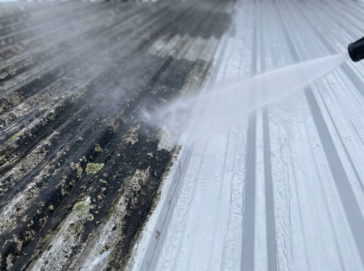 A dark roof being washed down with a wide fan of water