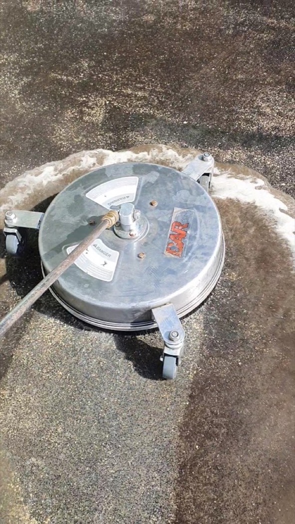A rotary surface cleaner taking the grime off an aggregate driveway