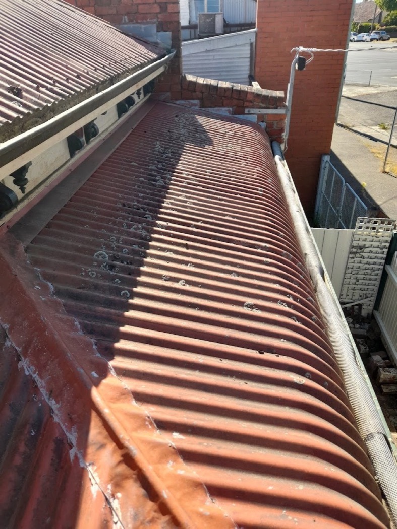 A box gutter beside a red corrugated iron roof, part way through being cleared and washed out