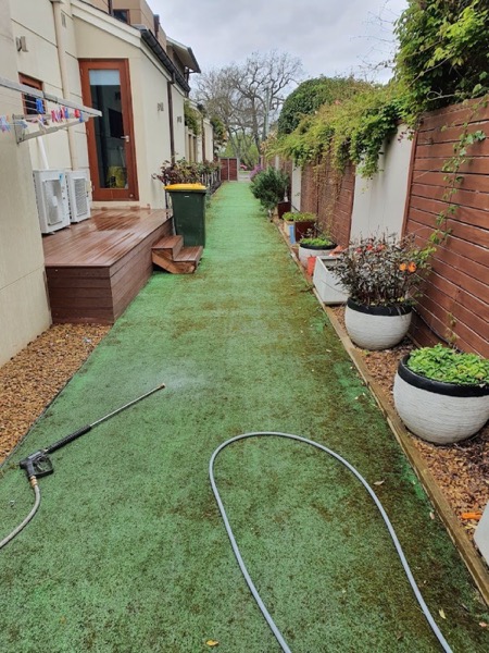 A synthetic grass path washed clean along a garden bed