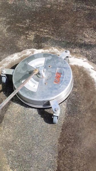 A rotary surface cleaner taking grime off an aggregate driveway