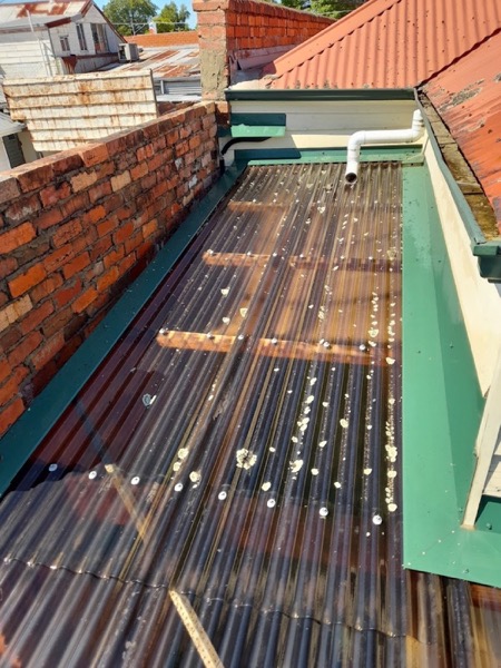 A translucent corrugated verandah roof between two brick walls, washed down